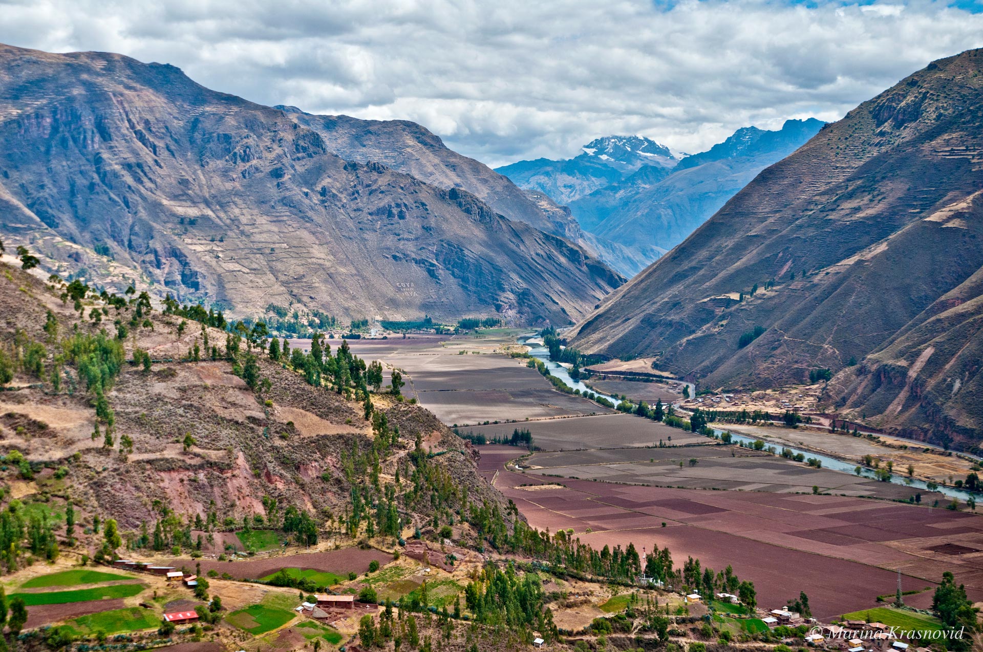 Sacred Valley of Incas Panoramic view of the Sacred Valley of the Incas, showing terraced farmland, the Urubamba River winding through the valley, and dramatic Andean mountain slopes rising in the background.