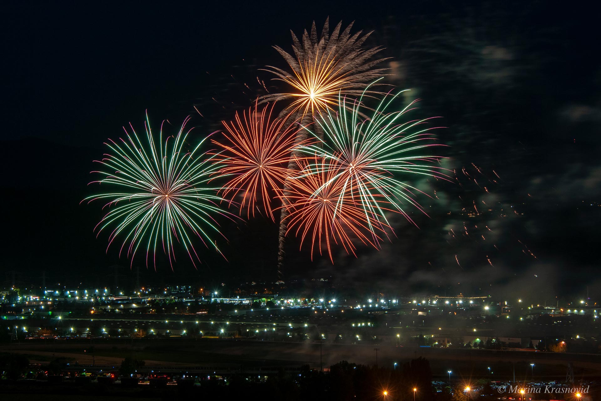 Colorful fireworks exploding over Green River Valley in Auburn, Washington, with city lights glowing beneath the night sky
