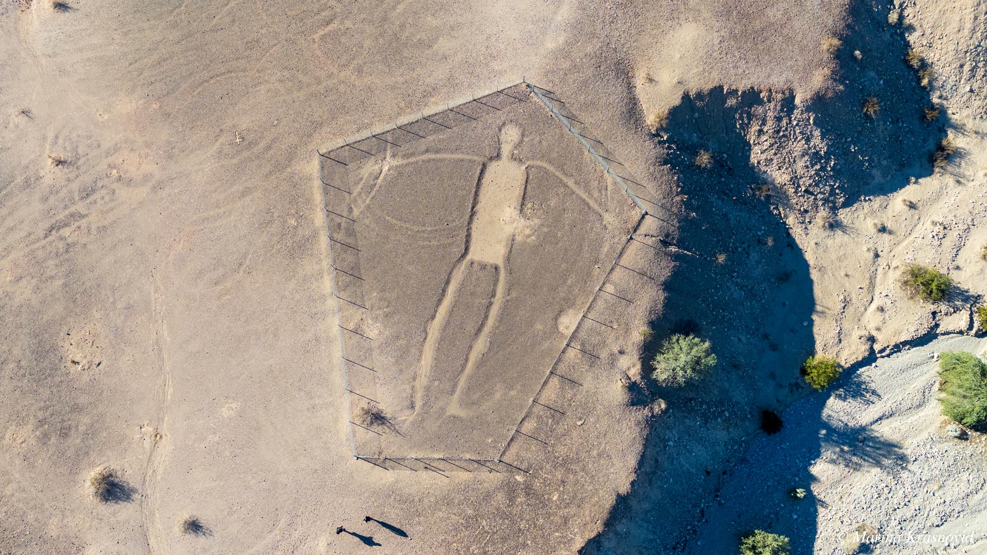 Aerial view of a large human-shaped Blythe Intaglio geoglyph in the Colorado Desert near Blythe, California, surrounded by a protective fence. Photographed by Marina Krasnovid.