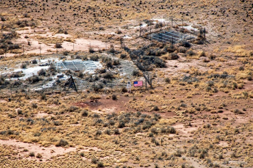 View of a fenced mining shaft entrance and a six-foot-tall astronaut figure on the floor of Meteor Crater, shown to illustrate scale at the bottom of the crater.