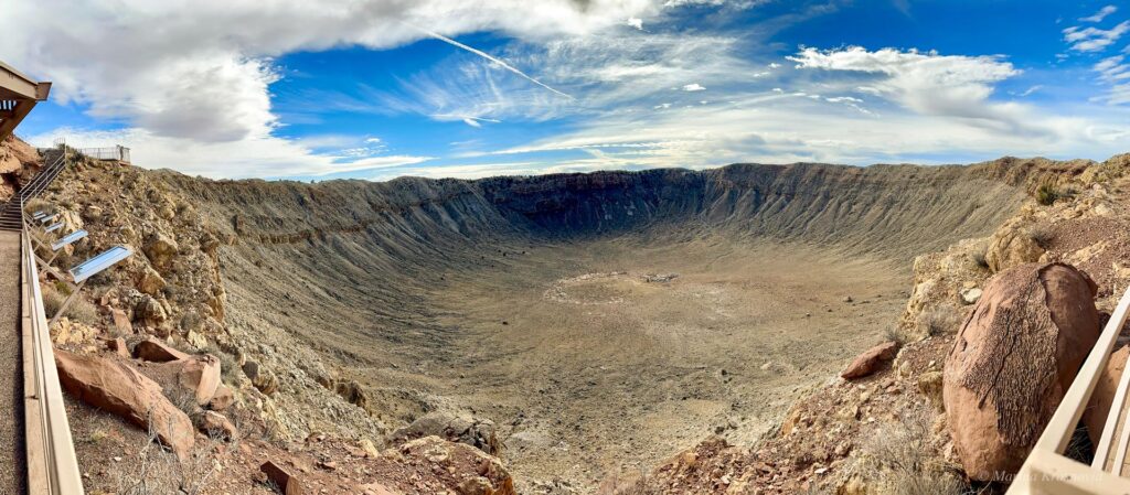 Panoramic view looking down into Meteor Crater in northern Arizona, showing the steep crater walls, rocky rim, and the flat crater floor below.