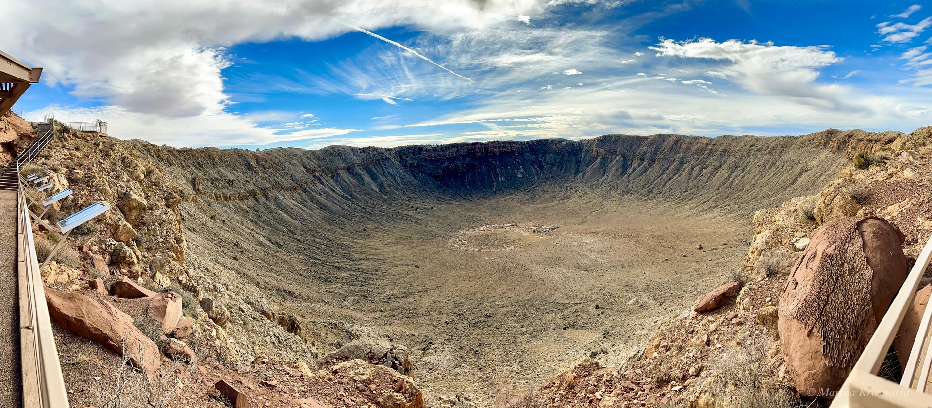 Panoramic view looking down into Meteor Crater in northern Arizona, showing the steep crater walls, rocky rim, and the flat crater floor below.